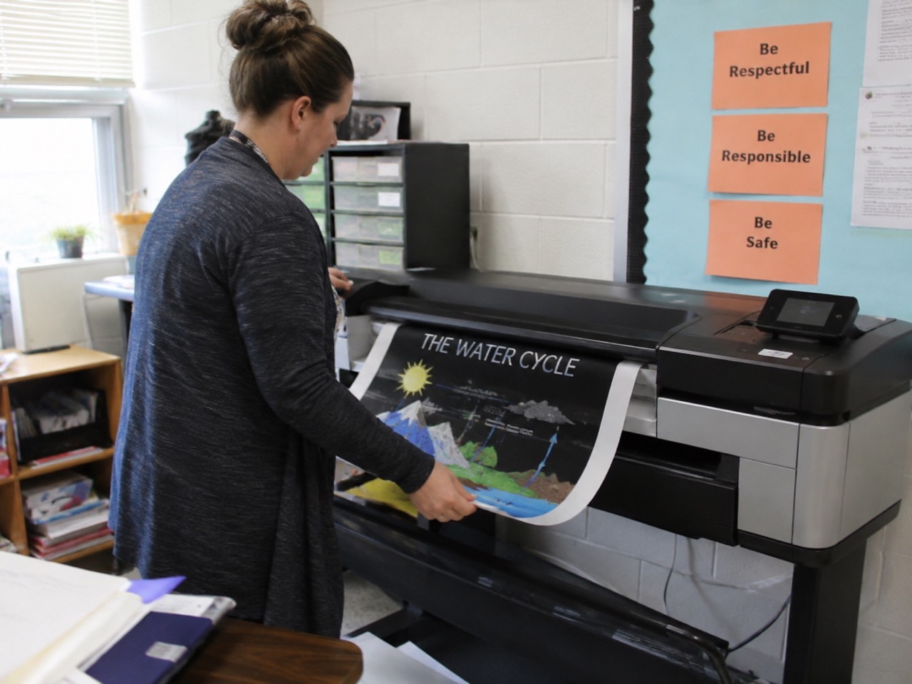 Teacher creating educational water cycle poster with poster making machine for schools